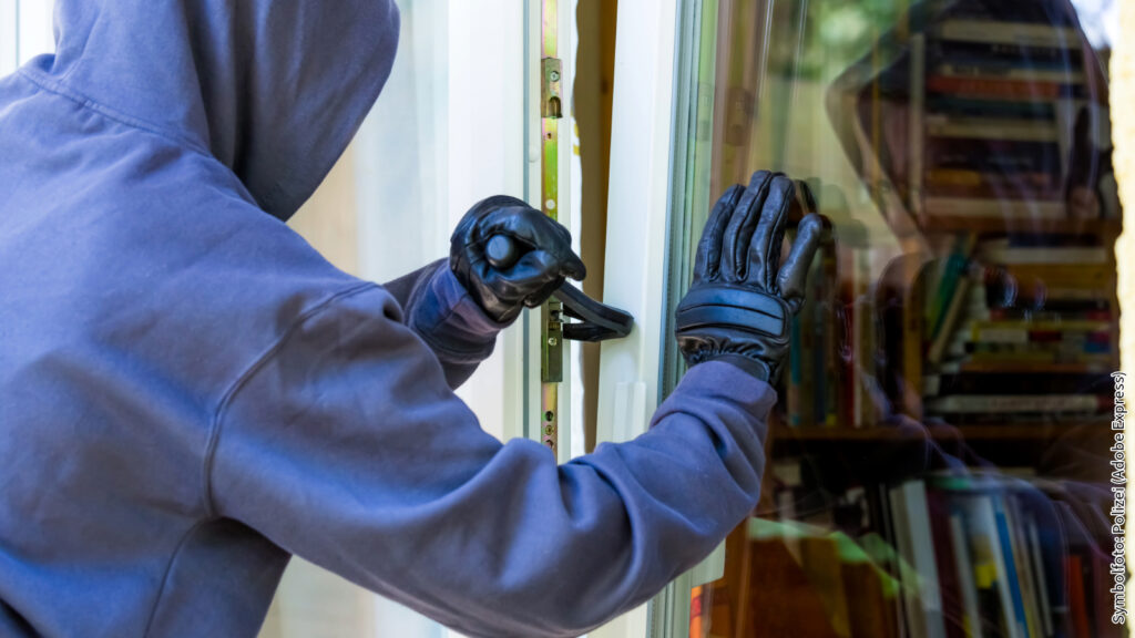 Einbrecher mit Kapuze und Handschuhen versucht, durch ein Fenster in ein Haus einzudringen.