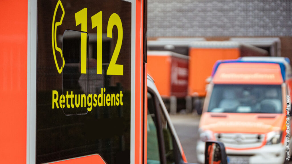 Rettungswagen mit der Notfallnummer 112 im Fokus, im Hintergrund weitere Rettungsdienstfahrzeuge auf einem Parkplatz.