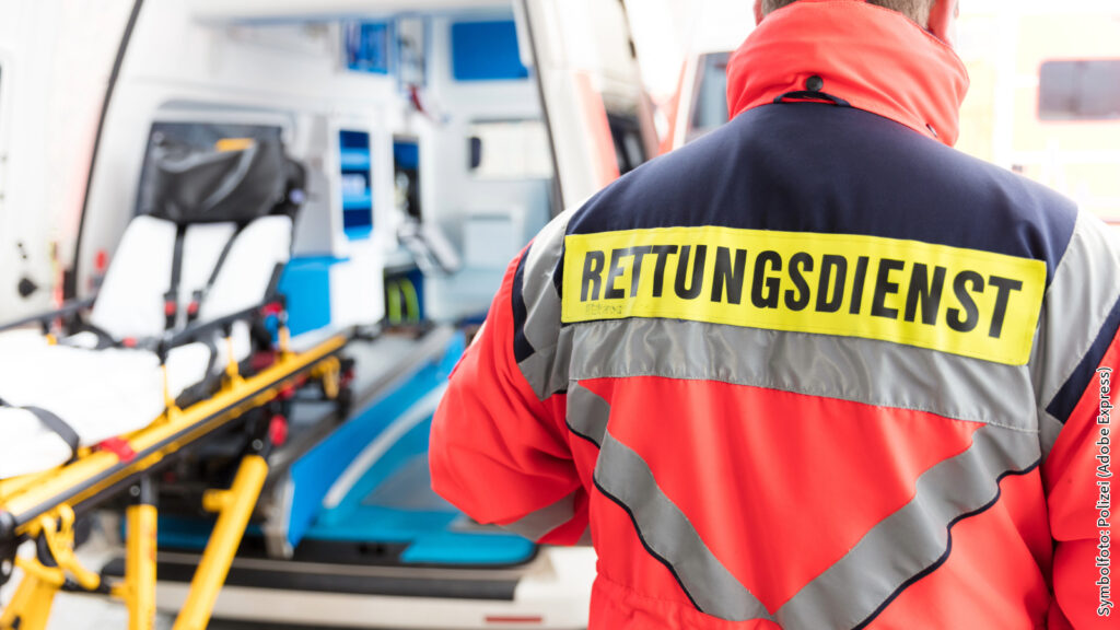 Rettungsdienst-Mitarbeiter vor Krankenwagen mit Trage im Hintergrund, bereit für den Einsatz bei Notfällen.