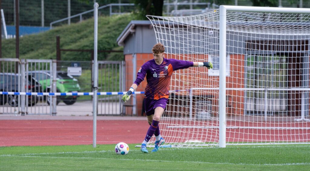 Ein Torwart in lila Trikot kickt den Ball im Fußballspiel, bereit für den Abstoß im Stadion.