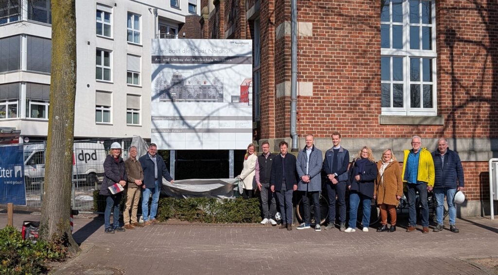Gruppe bei einer Baustellenbesichtigung vor der Musikschule Nordhorn, Neubauprojekt im Sonnenschein.