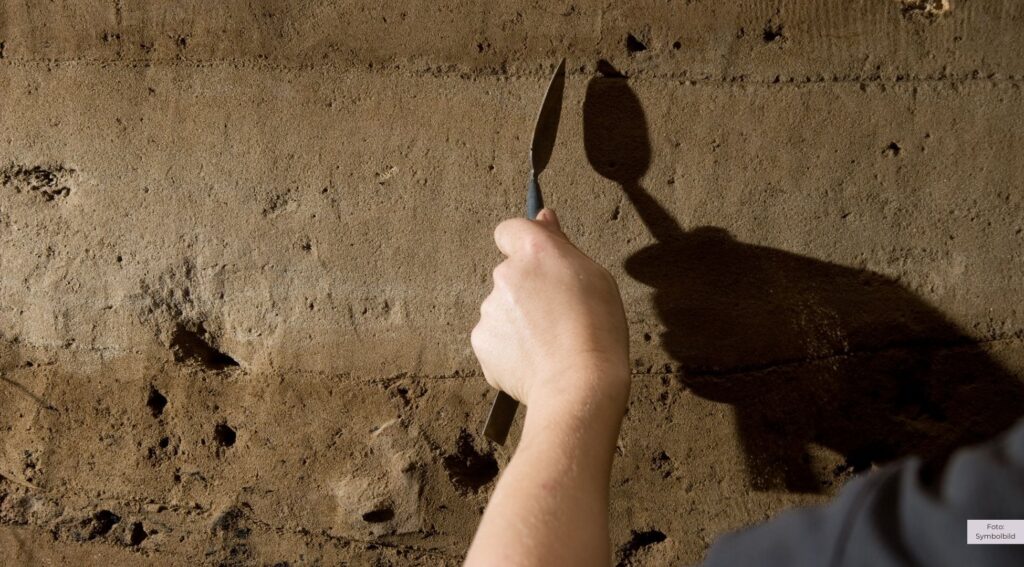 Hand gräbt mit Spachtel in eine Betonwand.