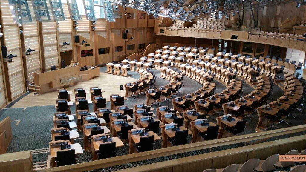 Moderner Sitzungssaal mit geschwungenen Sitzreihen und Holzelementen, leere Stühle und Tische in Parlamentsanordnung.