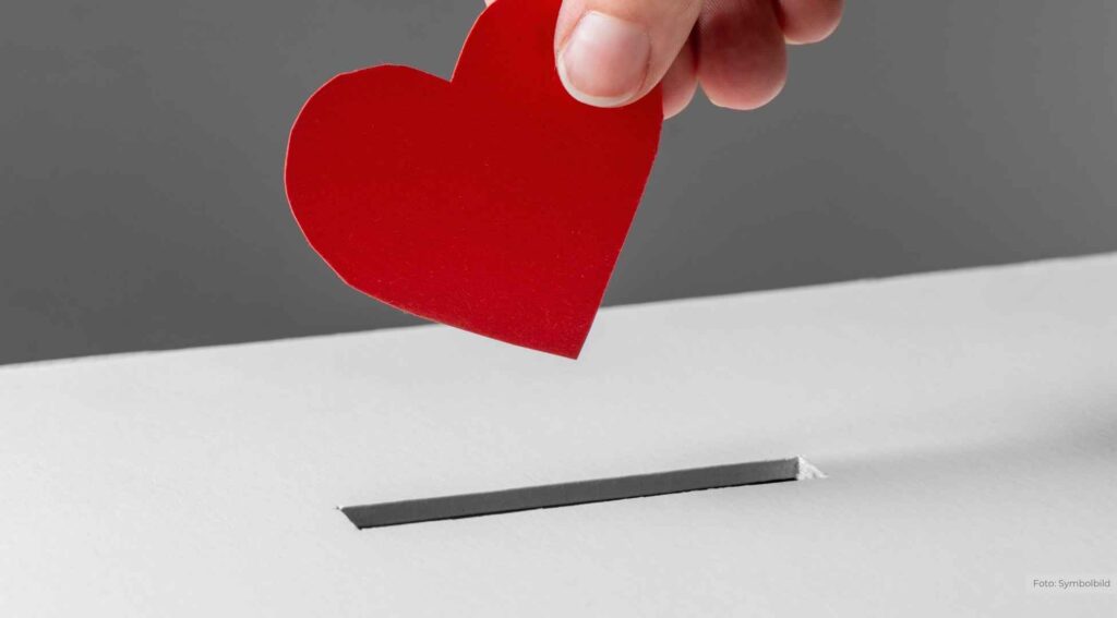 Rote Herzkarte wird in einen weißen Schlitz gesteckt – Symbol für Liebe und Spenden.