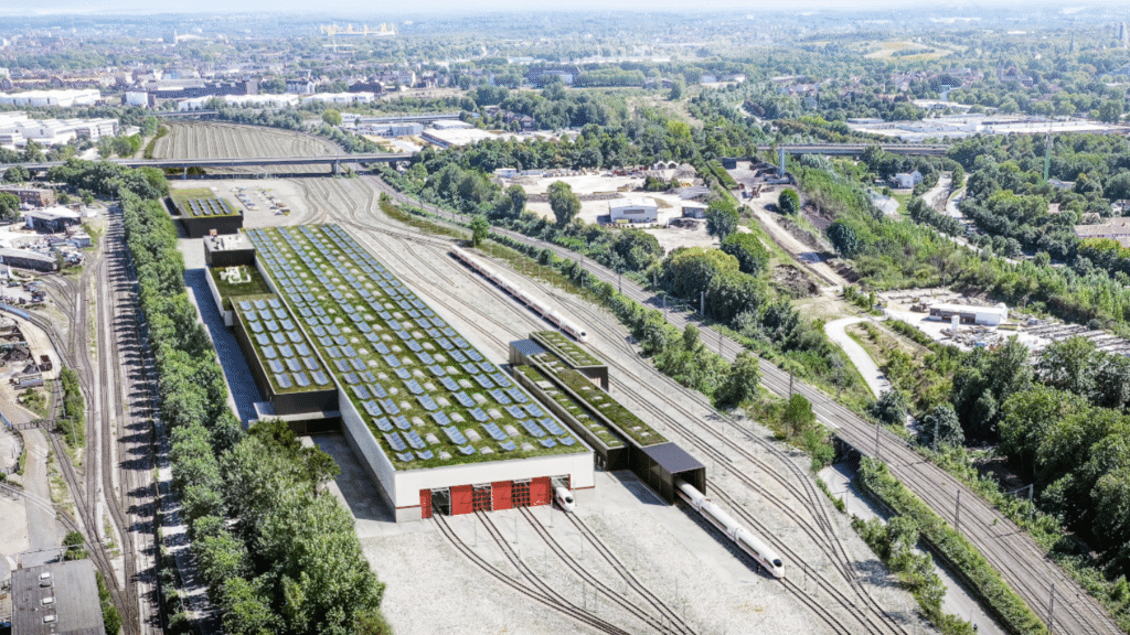 Luftbild eines großen, grünen Eisenbahndepots mit Solarzellen auf dem Dach und umgebenden Bahnstrecken in grüner Landschaft.