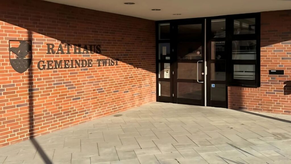 Eingang des Rathauses der Gemeinde Twist mit brauner Backsteinfassade und Glasfenstern, sonniger Tag.