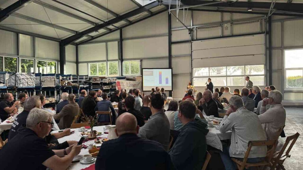 Menschen in einer Halle bei einem Seminar oder Workshop mit einer Präsentation auf einem Bildschirm.