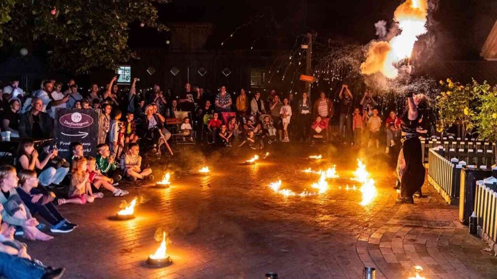 Feuerspucker-Show begeistert Publikum bei Nacht, umgeben von Feuerkreisen auf gepflastertem Platz.