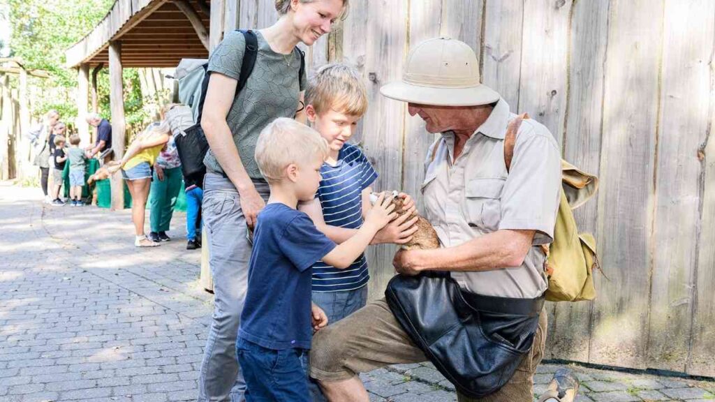 Familie begegnet Tierpfleger und streichelt ein Tier im Zoo, Kinder voller Neugier und Freude.