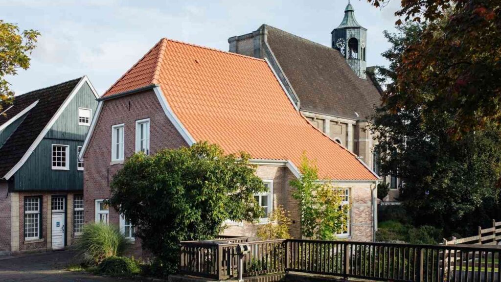 Traditionelles Backsteinhaus mit roten Ziegeln und Kirchturm im Hintergrund an einem sonnigen Herbsttag.