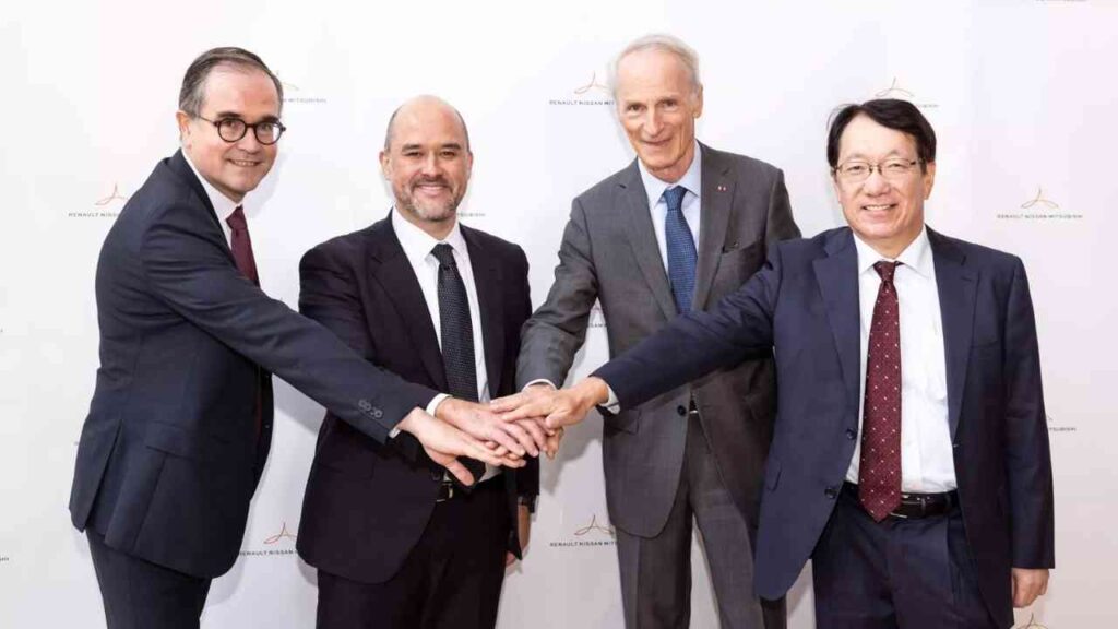 Geschäftsmänner im Anzug bei einer Zusammenkunft, vereinen Hände im Teamwork vor Renault-Nissan-Logo.