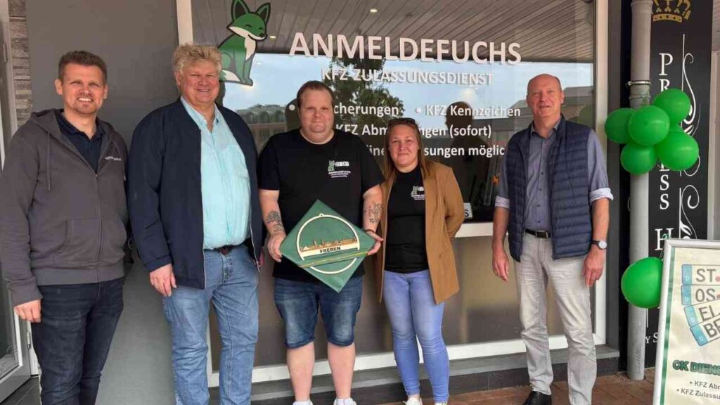 Gruppe von fünf Menschen vor dem Anmeldefuchs Kfz-Zulassungsdienst mit grünen Ballons und einem Schild.