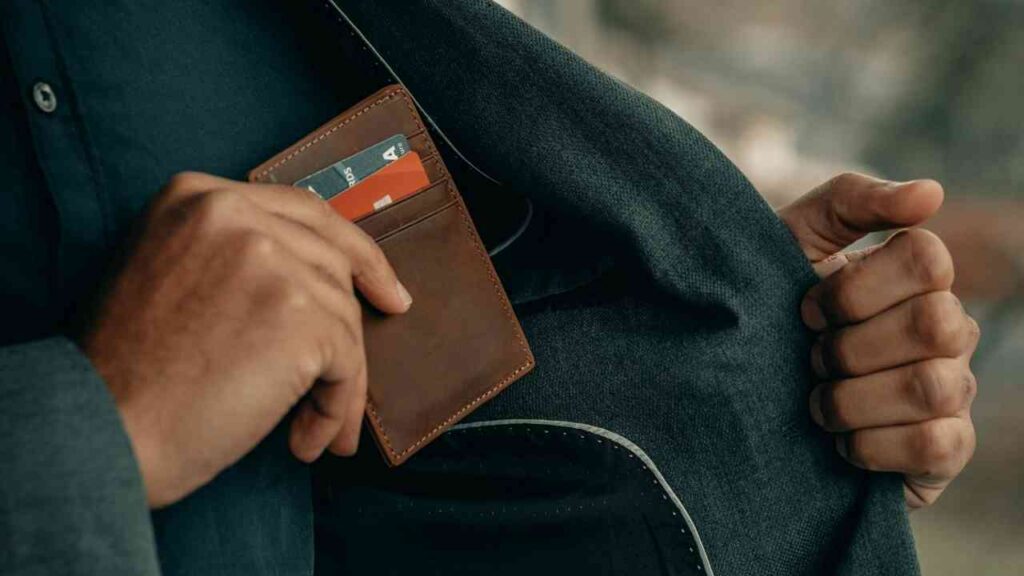 Mann zieht Geldbörse mit Kreditkarten aus einer Anzugtasche.