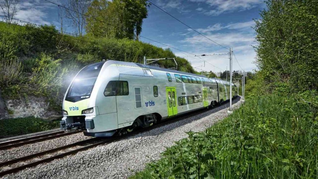 Moderner BLS-Regionalzug fährt durch grüne Landschaft bei strahlendem Sonnenschein, Schweiz.