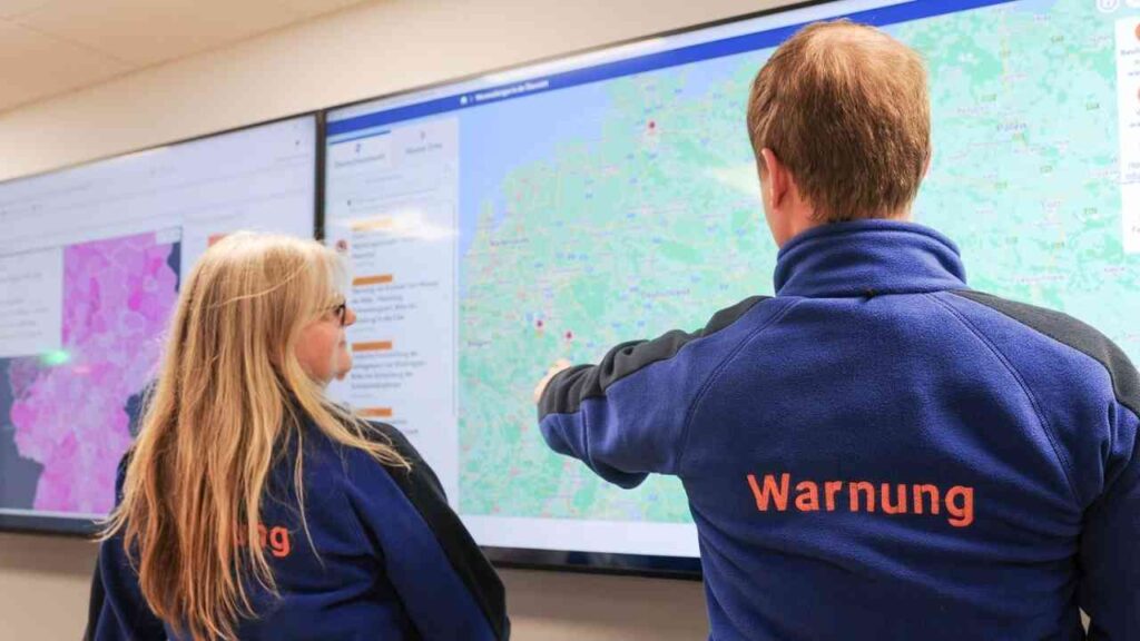 Zwei Personen analysieren Wetterdaten auf großen Bildschirmen im Warnzentrum.