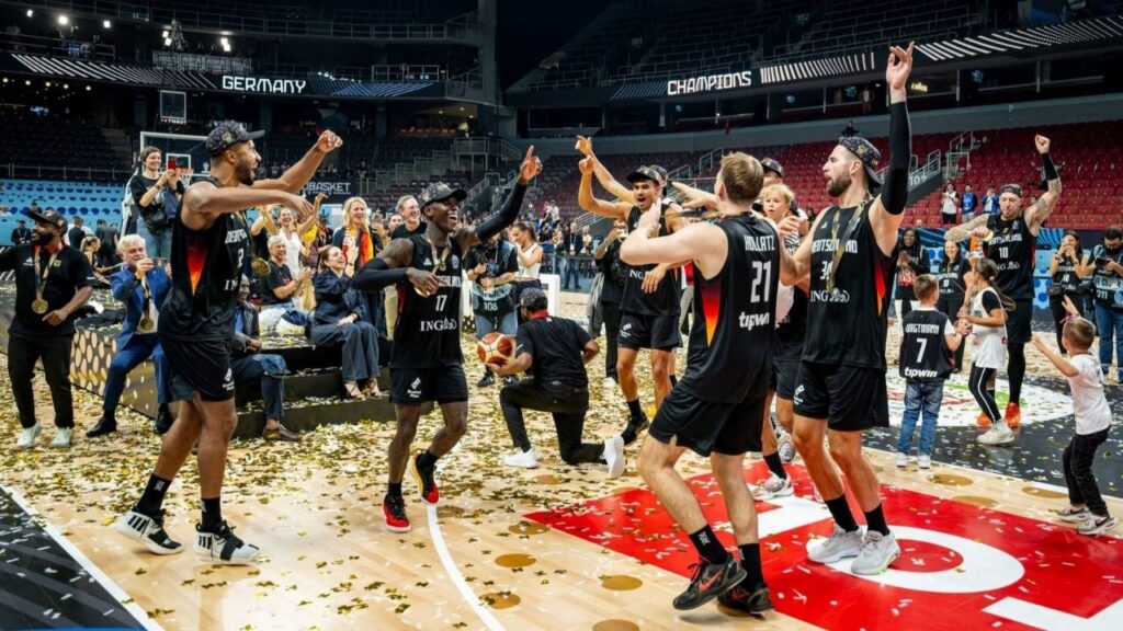 Basketballteam feiert jubelnd auf dem Spielfeld nach Turniersieg, umgeben von Fans und Konfetti.