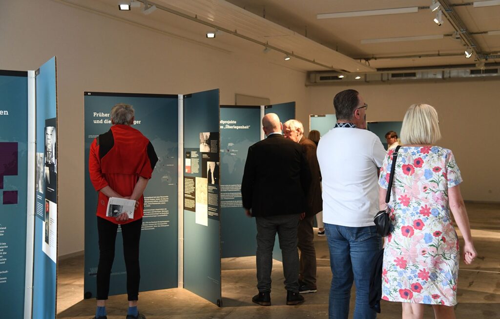 Besucher erkunden eine Ausstellung in einem modernen Museum mit beleuchteten Informationstafeln.