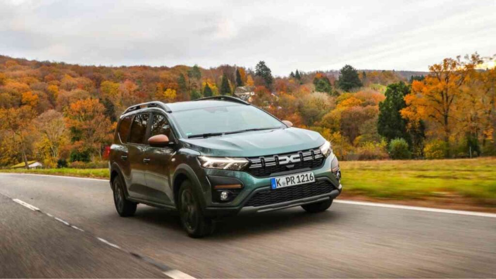 SUV auf Landstraße im Herbst, umgeben von buntem Laubwald, dynamische Fahrt bei bewölktem Himmel.