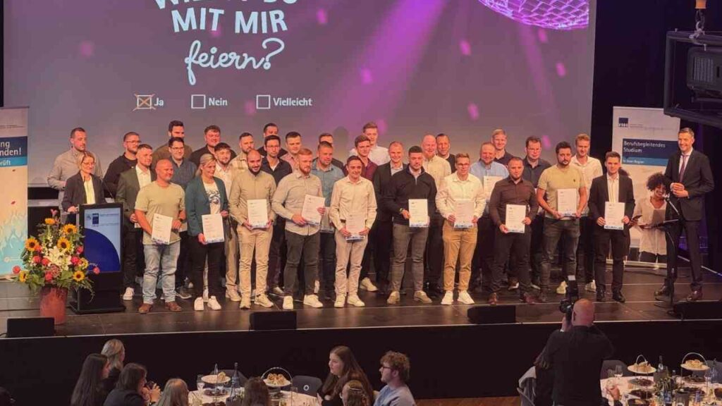 Gruppe von Absolventen auf einer Bühne bei einer Abschlussfeier, einige halten Zertifikate in den Händen.