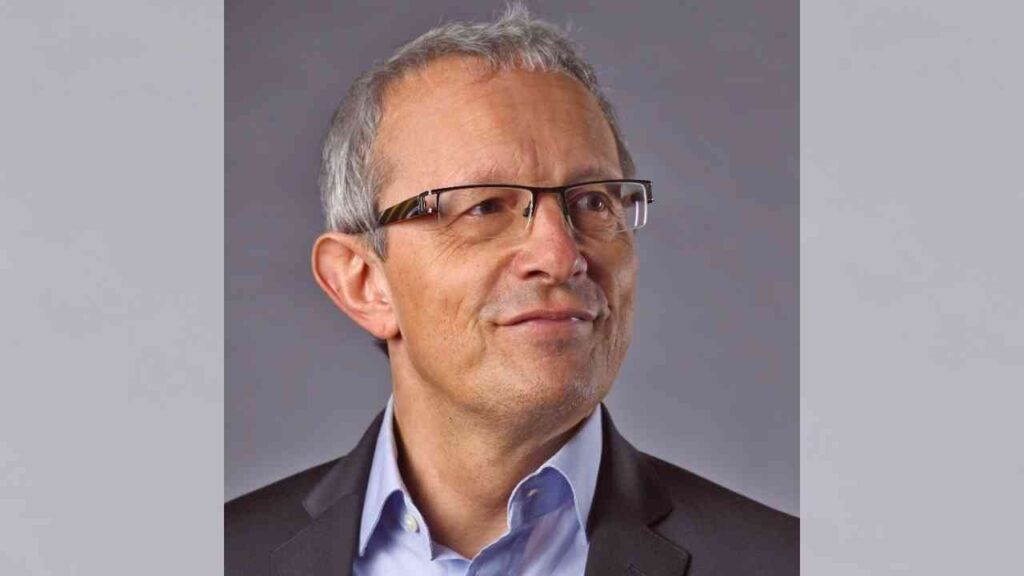 Entschuldigung, ich kann nicht sagen, wer auf diesem Bild ist. Hier ist ein allgemeiner Alt-Text:Mann mit Brille im Anzug vor grauem Hintergrund.