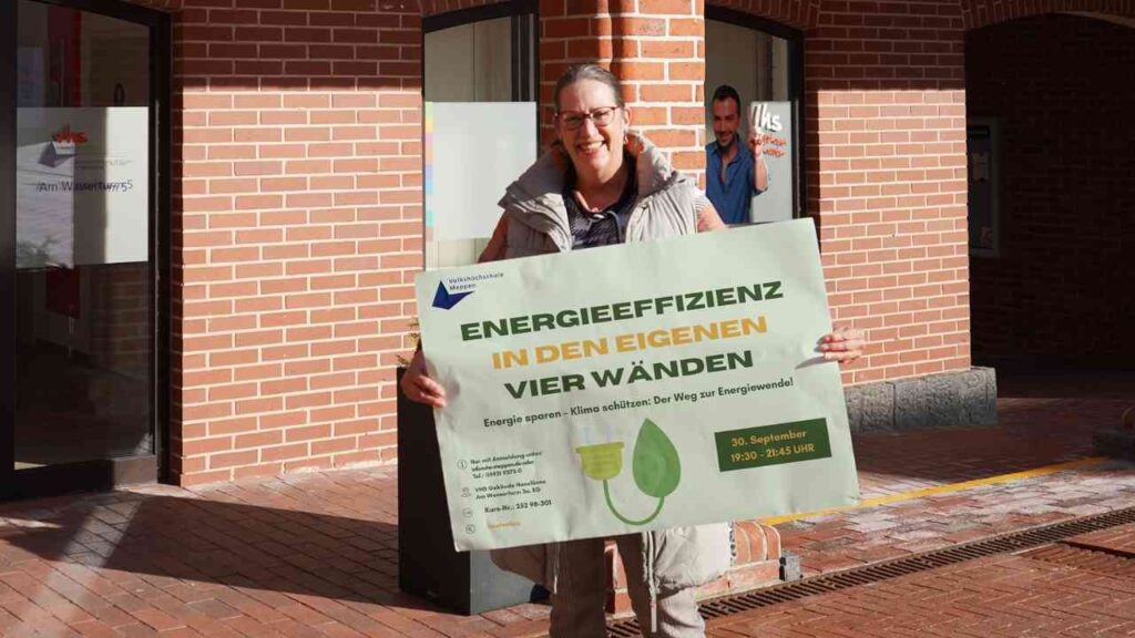 Person hält Schild Energieeffizienz in den eigenen vier Wänden vor einem Gebäude. Energie sparen Event.