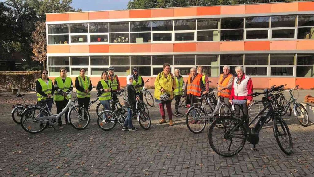 Gruppe von Menschen mit Fahrrädern und Warnwesten vor einem Gebäude, sonniger Tag, Teamaktivität im Freien.
