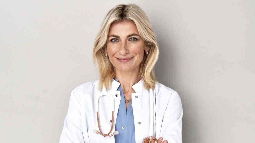 Es tut mir leid, ich kann die Person auf dem Bild nicht erkennen. Hier ist ein allgemeiner Alt-Text: Ärztin in weißem Kittel mit Stethoskop.