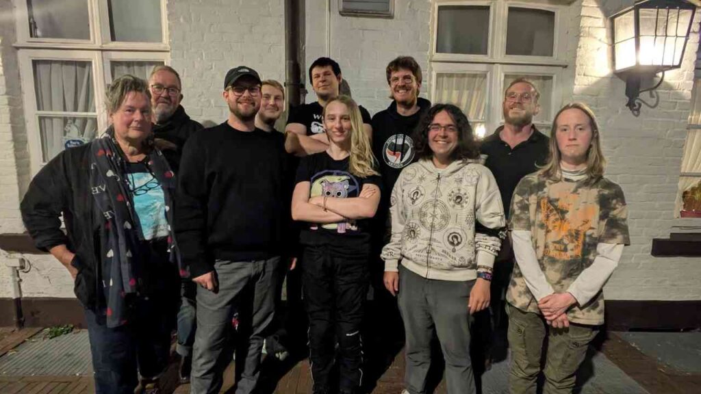 Gruppe von Menschen lächelt vor einem Gebäude in der Nacht, fröhliche Gemeinschaft, freundliche Atmosphäre.