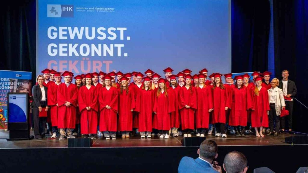 Absolventen in roten Roben bei IHK-Zeremonie, vor Banner mit Gewusst. Gekonnt. Gekürt.