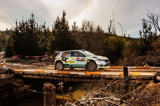Rallyeauto überquert hölzerne Brücke in bewaldeter Landschaft bei Rennveranstaltung.