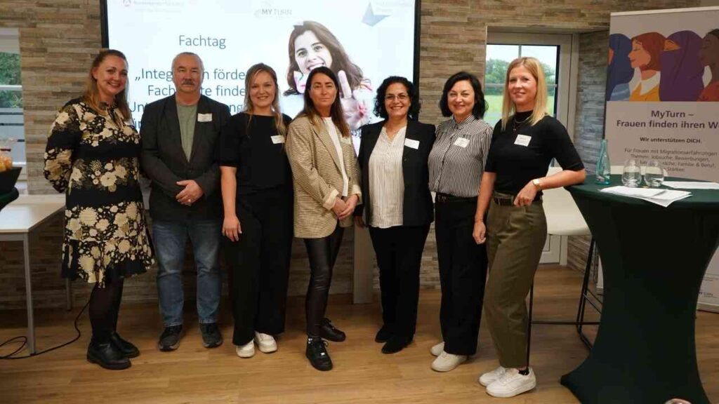 Gruppe von Menschen beim „Fachtag Integration fördern“ Event in einem Raum mit Präsentation im Hintergrund.
