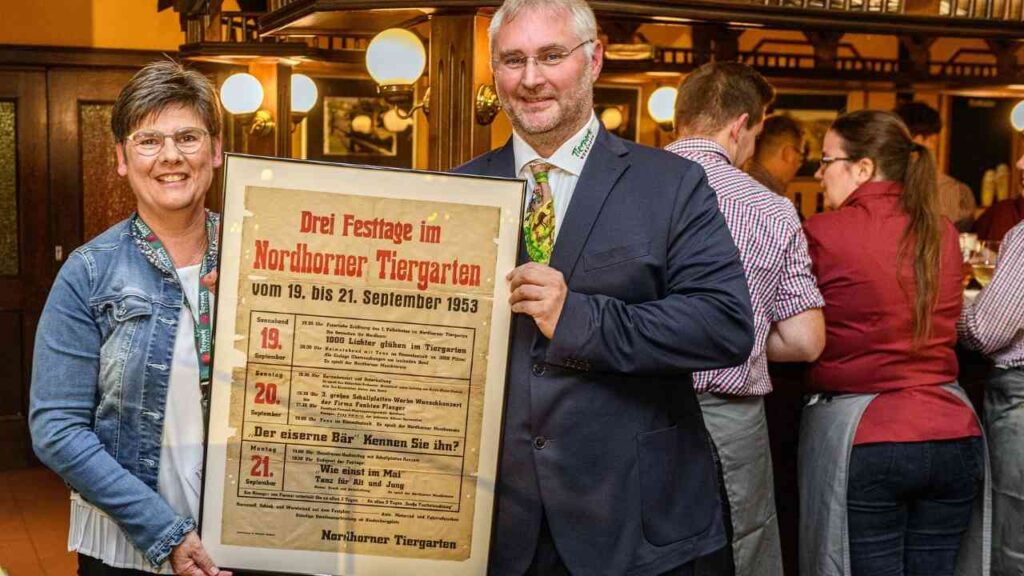 Personen mit historischem Plakat Drei Festtage im Nordhorner Tiergarten, 1953 in einem Restaurant.