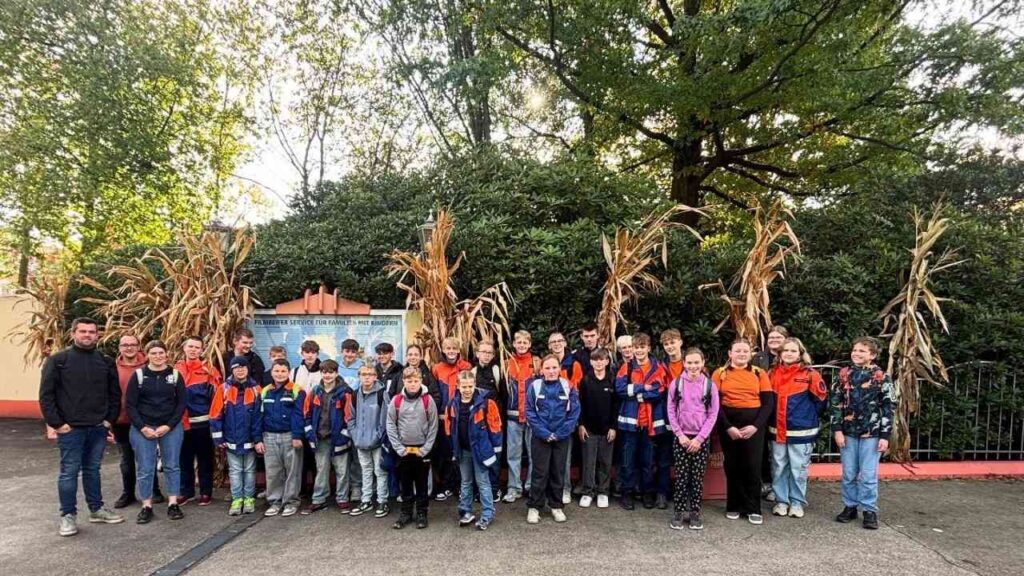 Gruppe von Kindern in bunter Kleidung posiert vor Herbstkulisse mit Bäumen und Stroh für ein Gruppenfoto.