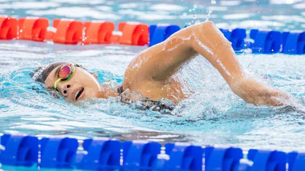 Eine Schwimmerin im Wettkampf schwimmt Kraulstil im Pool mit bunten Schwimmbrillen.