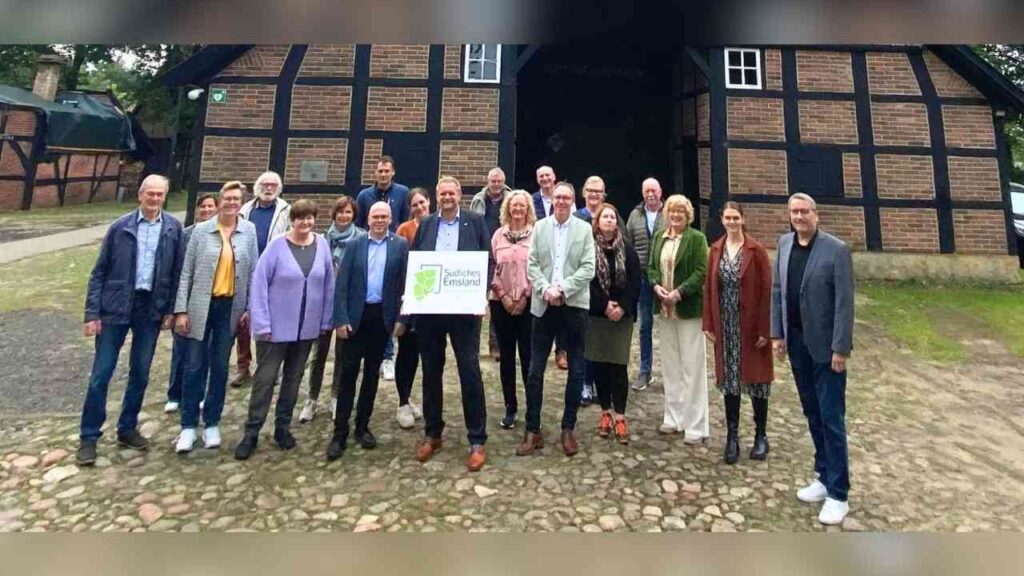 Gruppe von Menschen vor einem alten Backsteingebäude, hält ein Schild mit Südliches Emsland darauf.