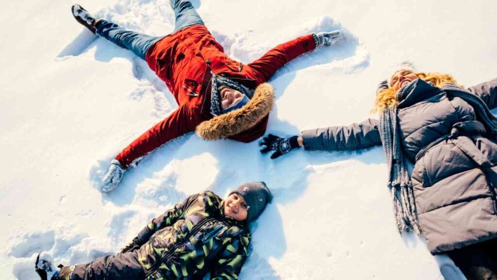 Menschen in Winterkleidung machen Schneeengel im Schnee, voller Freude und Lachen an einem sonnigen Wintertag.