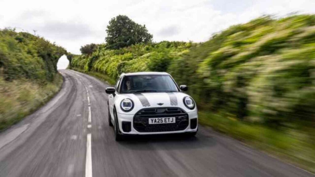 Weißes Auto auf landschaftlicher Landstraße, umgeben von hohen, grünen Hecken, bei bewölktem Himmel.