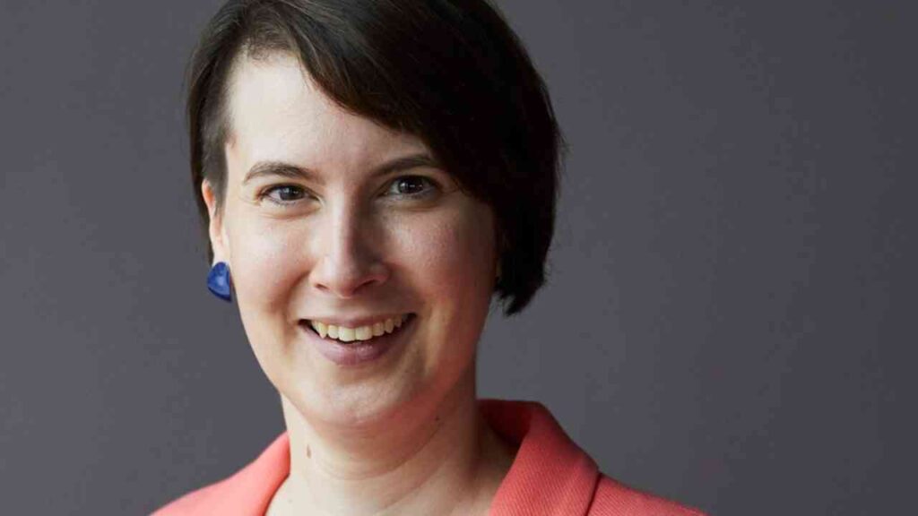 Ich kann die Person auf dem Bild nicht identifizieren. Deshalb wäre ein neutraler Alt-Text: Lächelnde Frau mit dunklem Haar und blauem Ohrring.