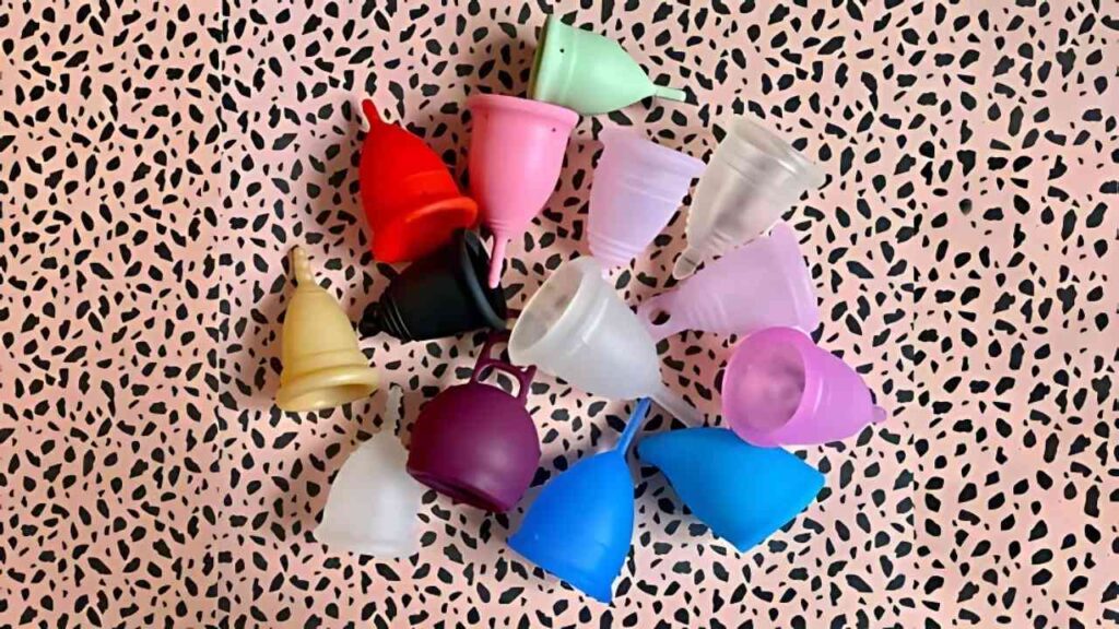 Bunte Menstruationstassen auf gemustertem Hintergrund für nachhaltige Monatshygiene.
