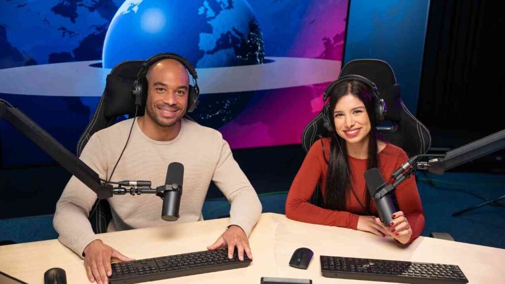 Zwei Podcaster moderieren eine Live-Sendung im Studio, sitzen vor Mikrofonen und Computern.