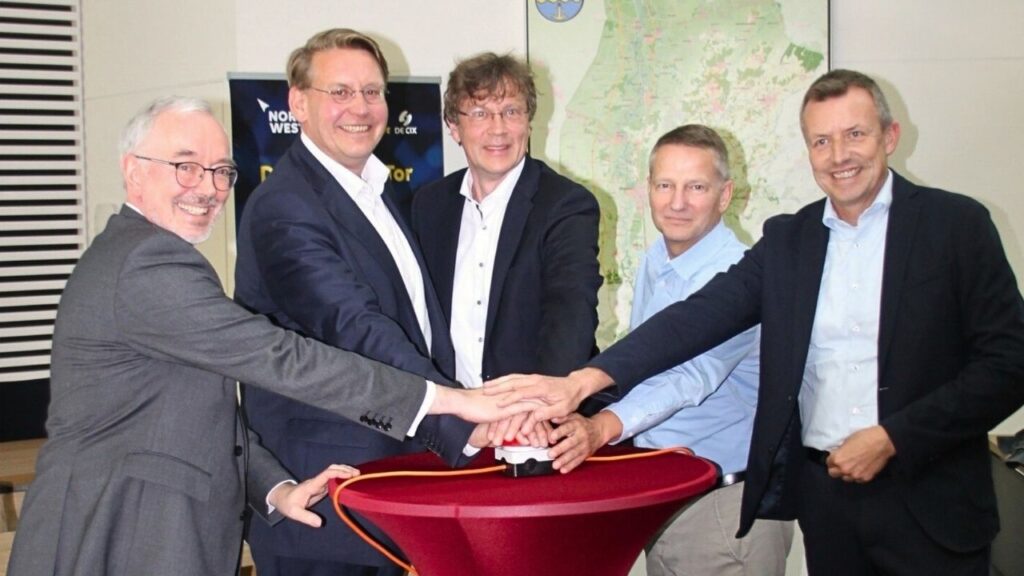 Gruppenvon Männern drückt gemeinsam einen großen roten Knopf bei einem Event, lächeln in die Kamera.