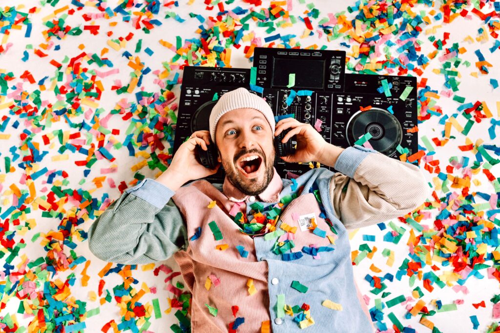 DJ feiert auf einem bunten Konfettiboden mit Musik und Kopfhörern, voller Freude und Energie.