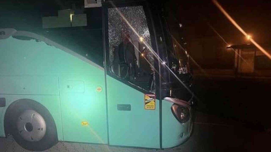 Grüner Reisebus bei Nacht mit beschädigter Fensterscheibe, geparkt an einer Bushaltestelle.