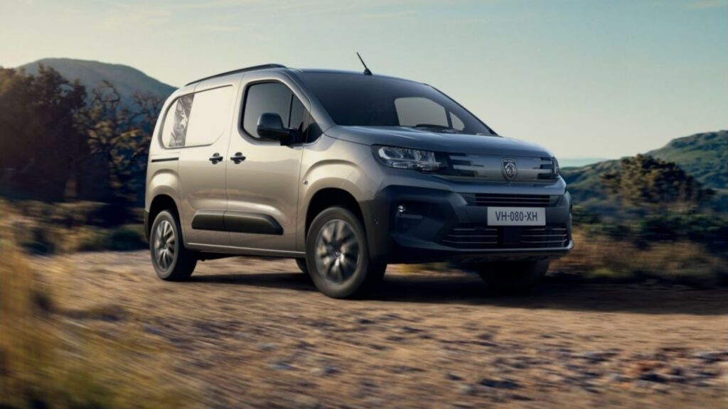 Grauer Lieferwagen fährt auf ländlicher Straße bei Sonnenuntergang, Berge im Hintergrund.