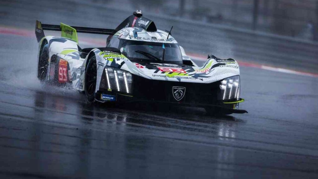 Rennwagen auf nasser Strecke, spritzendes Wasser, dynamisches Fahrverhalten, Peugeot-Logo deutlich erkennbar.