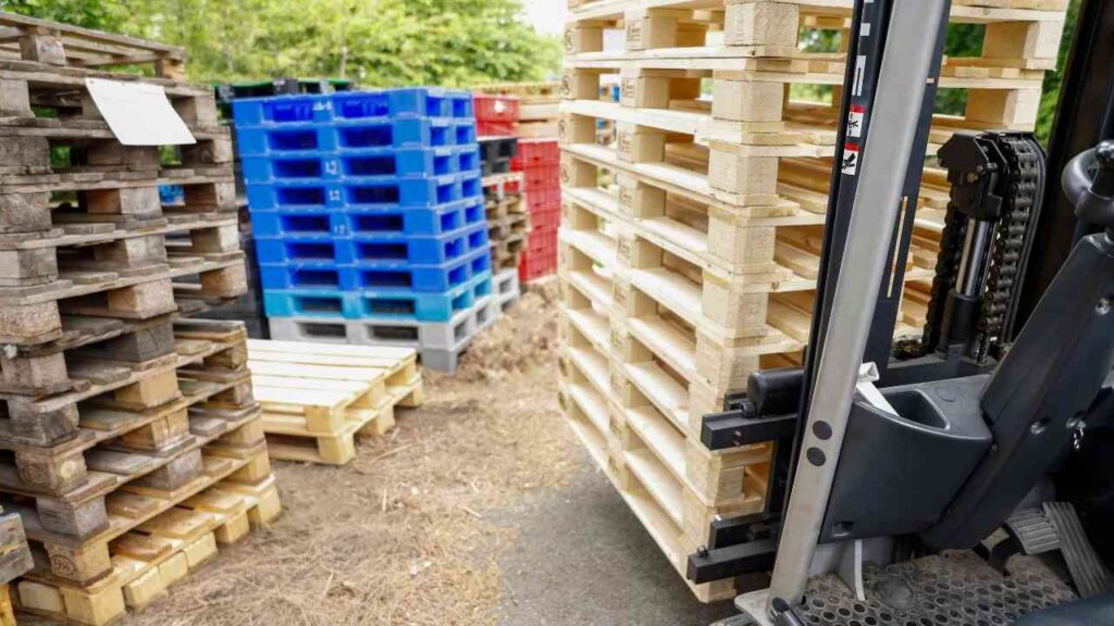 Gabelstapler bewegt gestapelte Holzpaletten auf Lagerplatz, umgeben von farbigen Paletten. Logistik und Materialwirtschaft.