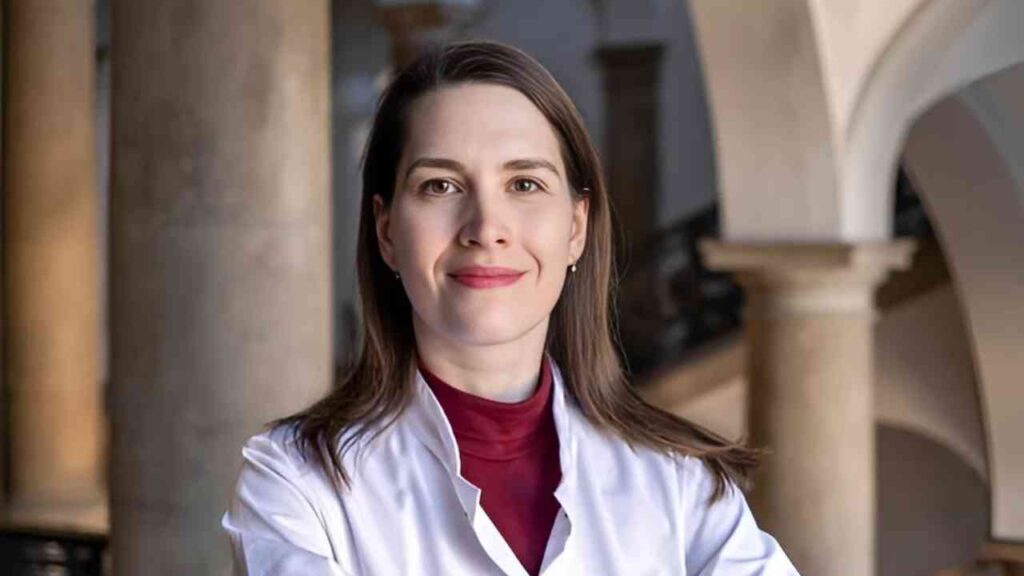 Portrait einer lächelnden Frau im weißen Kittel in einem historischen Gebäude.