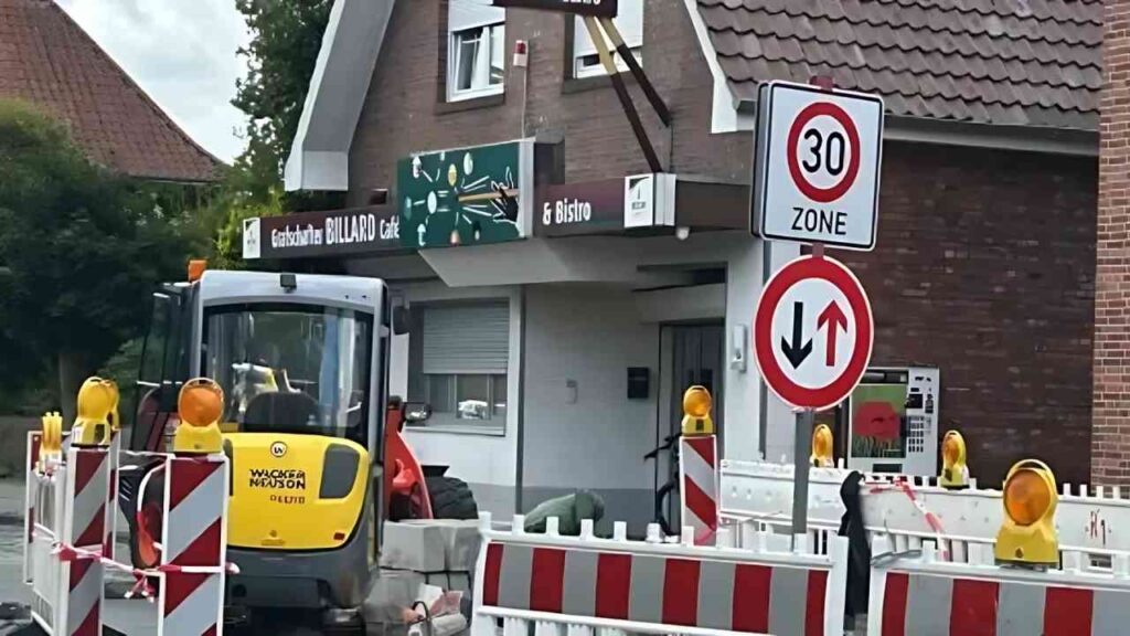 Straßenbauarbeiten vor einem Billard Café in einer 30er Zone mit Bagger und Verkehrsschildern.