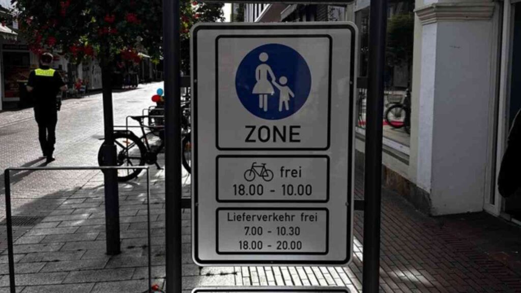 Fußgängerzone-Schild mit Rad- und Lieferverkehrszeiten in einer belebten Straße, Fahrräder 18-10 Uhr, Lieferung 7-10:30, 18-20 Uhr.