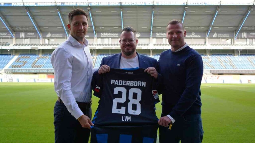 Drei Männer im Fußballstadion halten ein SC Paderborn Trikot mit der Nummer 28.